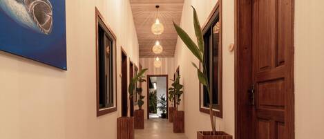 Un pasillo con puertas de madera, plantas en macetas y lámparas colgantes.