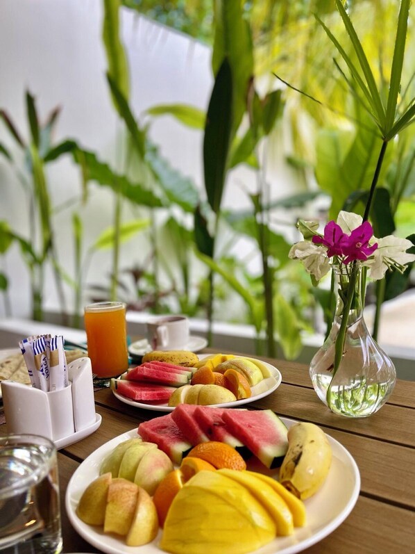 A table with plates of fruit, a glass of orange juice, a vase with flowers, and a cup of coffee. - Oasis Dhigurah (Dhigurah)