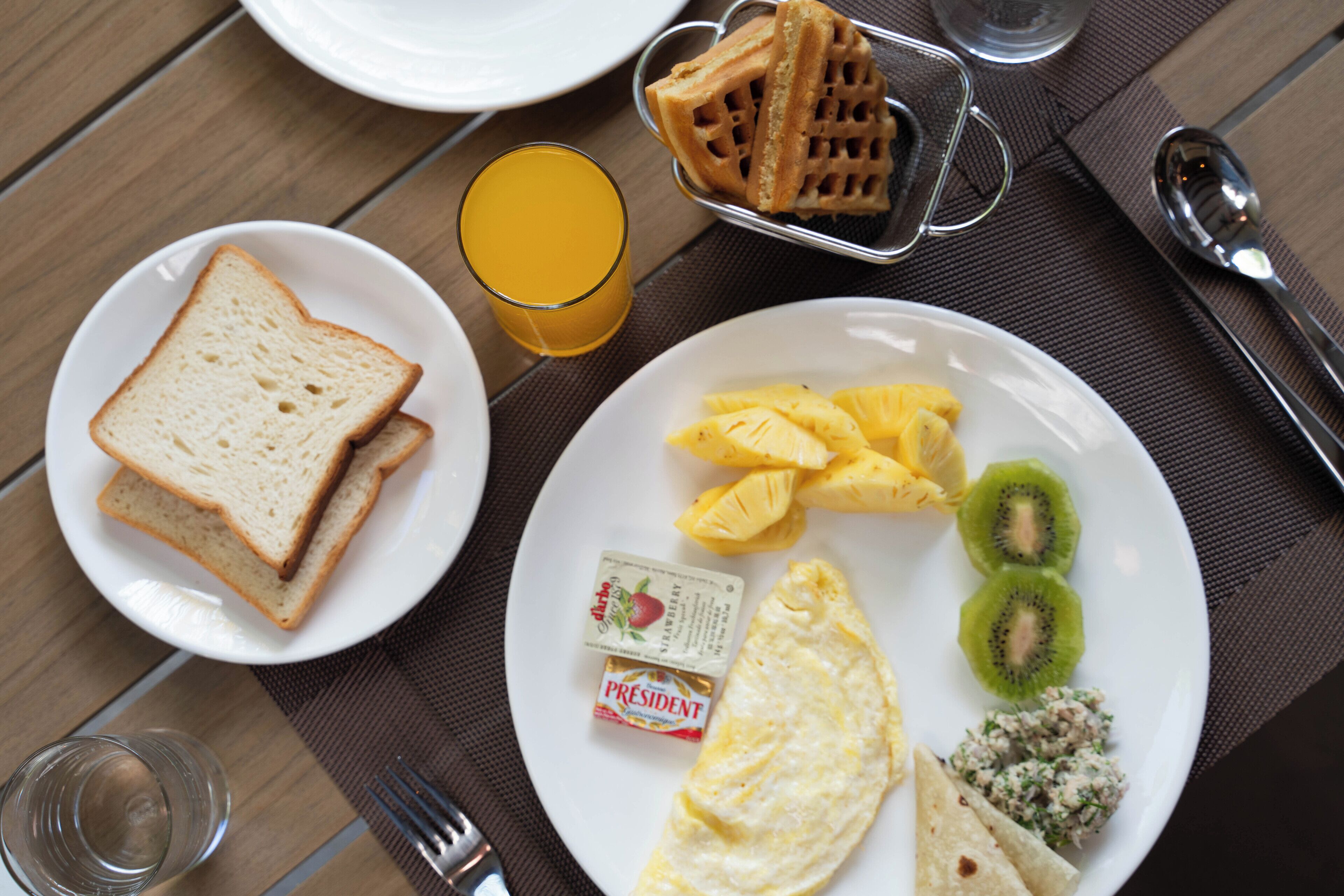 Desayuno con tostadas, gofres, kiwi, piña, huevos revueltos y un pequeño recipiente de mermelada.