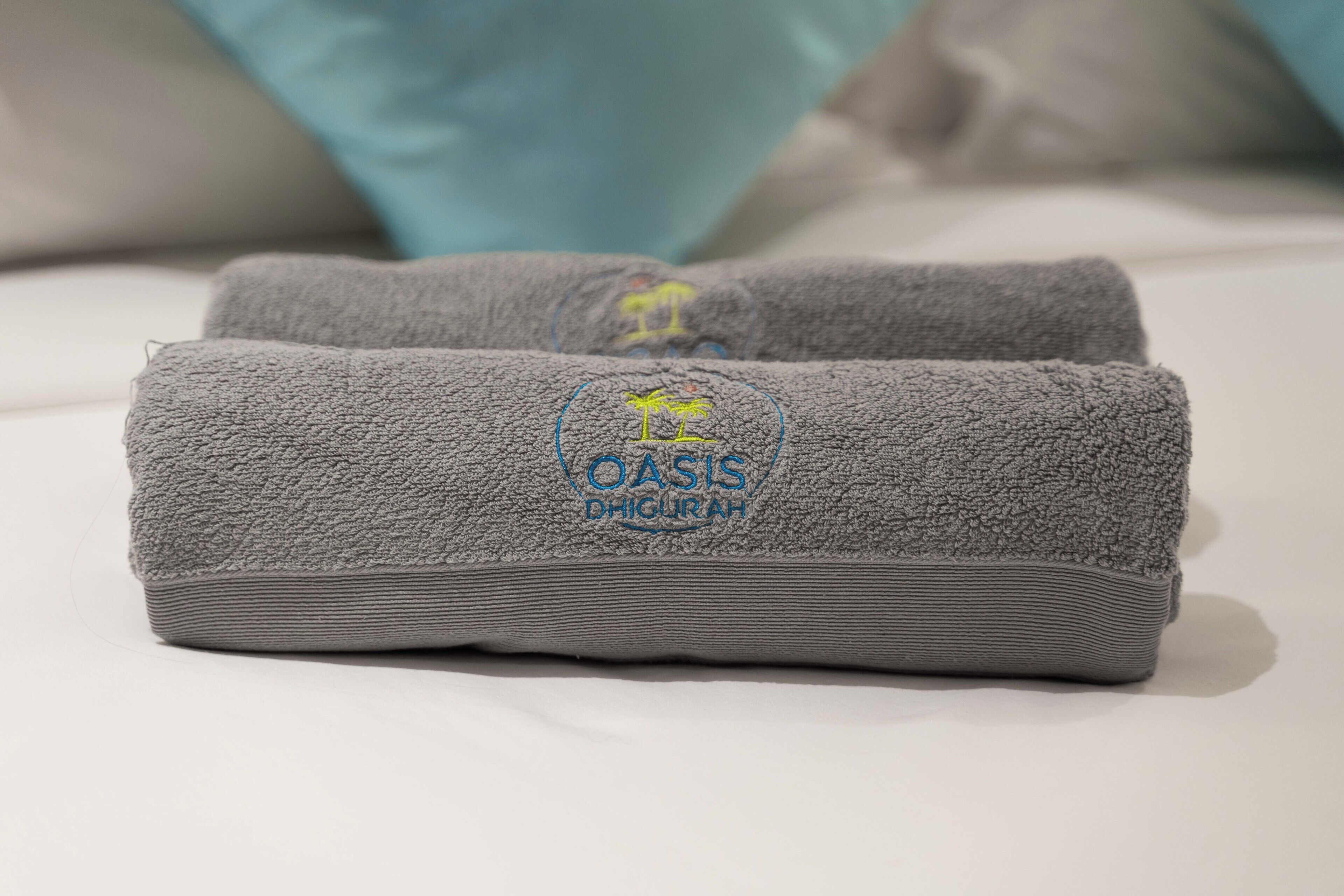 Two grey towels with a logo and text on a bed.