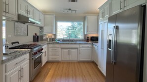 A modern kitchen with white cabinetry, a stainless steel refrigerator, and a large window providing natural light.