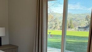 A bedroom with a large bed, a bedside table, and a view of a green landscape through a sliding glass door.