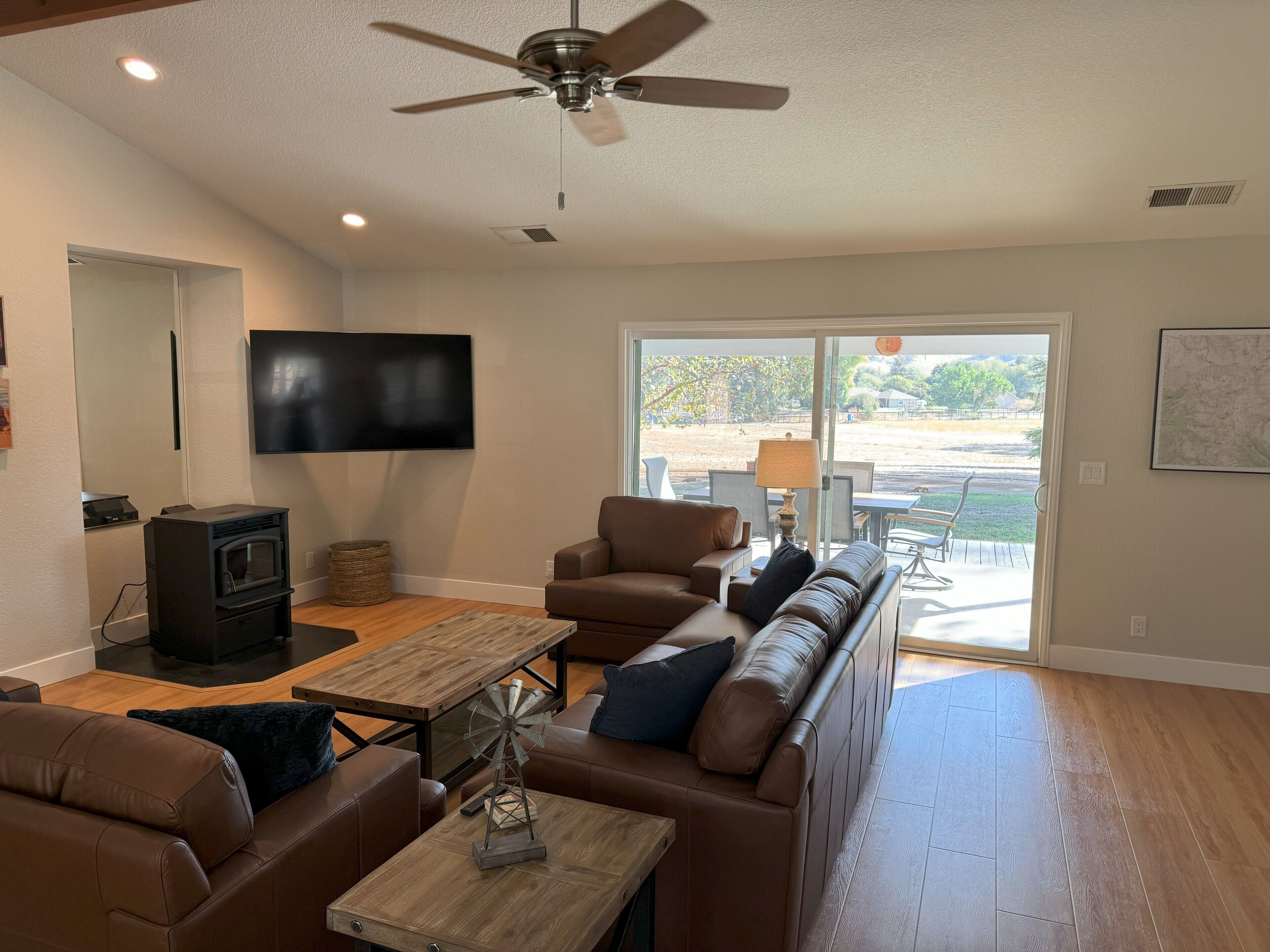 A modern living room with a flat-screen TV, a fireplace, leather sofas, a wooden coffee table, and a ceiling fan.