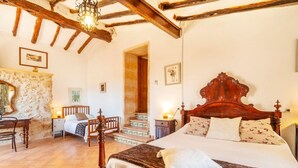 Une chambre avec un grand lit, des poutres en bois, un mur en pierre et un escalier.