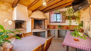 Un coin repas rustique avec un four en briques, des poutres en bois et des plantes en pot.