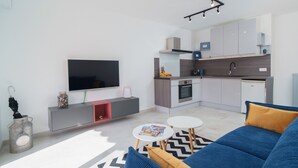 A modern living room with a blue sofa, a flat-screen TV, a small kitchen area, and a dining table. - 2 Rooms Air-conditioned near Cannes beaches (Le Cannet)