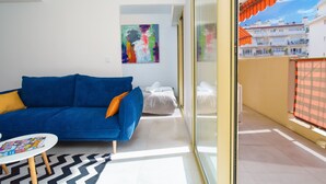 A modern living room with a blue sofa, a small round table, and a colorful abstract painting on the wall. - 2 Rooms Air-conditioned near Cannes beaches (Le Cannet)