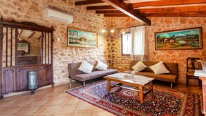 Une pièce rustique aux murs de pierre, avec des poutres apparentes, deux canapés, une table basse et un tapis à motifs.