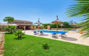 Un espace piscine aménagé avec des chaises longues, des parasols et un bâtiment doté d’un toit en tuiles.