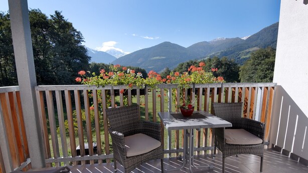 Een balkon met rieten stoelen, een tafel en uitzicht op bergen.