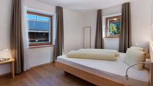 Een slaapkamer met een bed, nachtkastje, raam met gordijnen, spiegel en uitzicht.