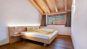 A bedroom with a wooden ceiling, a bed with a white mattress and yellow bedding, a bedside table with a lamp, and a window with curtains. - Apartment 'Hausergut Bonita 1' with Mountain View, Shared Garden and Wi-Fi (Sluderno)