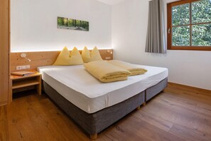 A bedroom with a bed, a nightstand, a wall-mounted light, a window with curtains, and a picture on the wall.