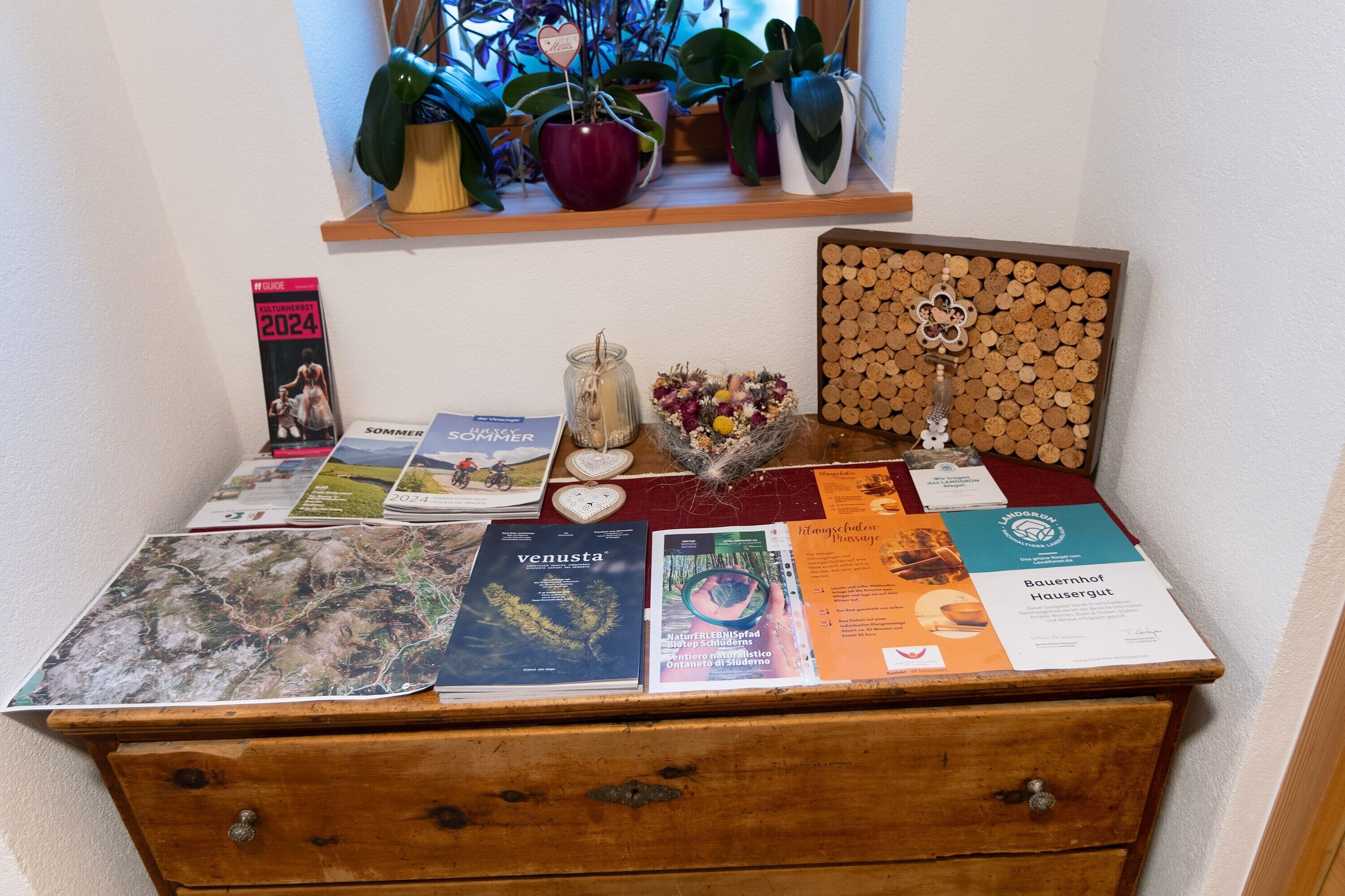 A wooden desk with various items including books, a glass jar with flowers, and a corkboard.