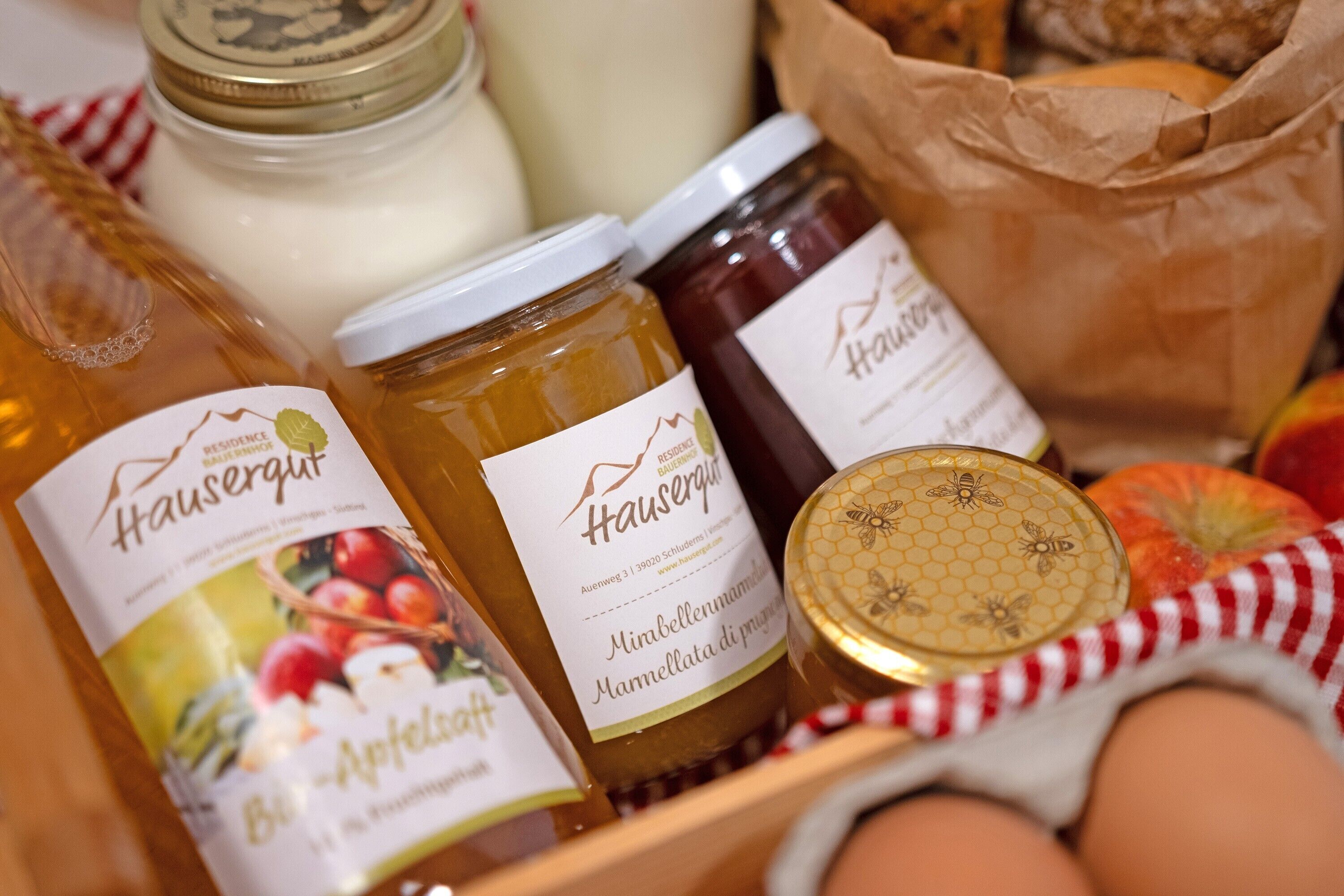 A variety of food items including jars of honey, a bottle of milk, and eggs, arranged on a wooden surface with a red and white checkered cloth underneath.