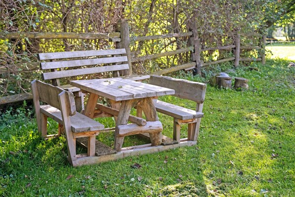 A wooden bench and picnic table in a grassy area with a wooden fence in the background.