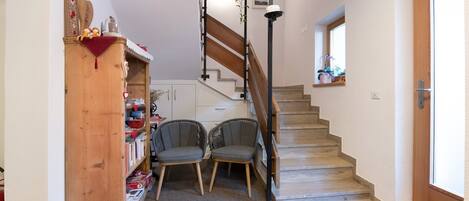 A staircase leading to a second floor, a wooden cabinet with books, two chairs, and a small window with a view.