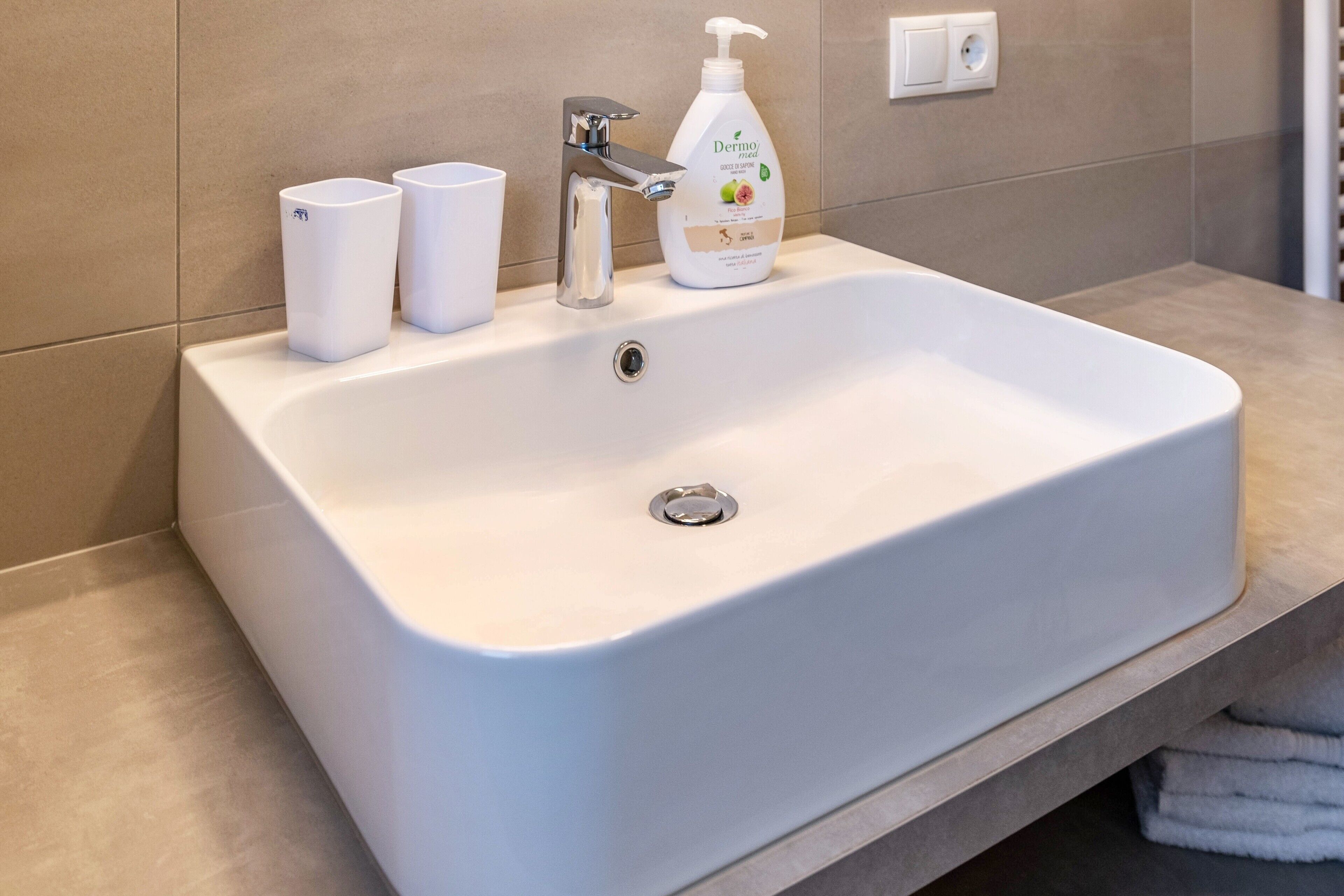 Een badkamer met een witte wastafel, een kraan, een zeepdispenser en twee witte bekers.
