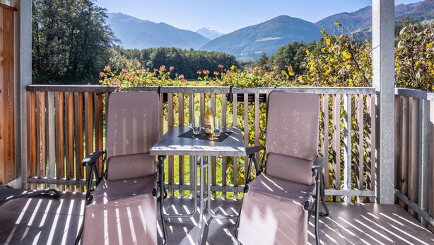 Een balkon met een tafel en stoelen, een fles en een glas, met uitzicht op een bergachtig landschap.