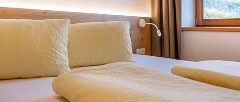 Habitación de hotel con cama, almohadas, una lámpara de noche y una ventana con vistas a las montañas.