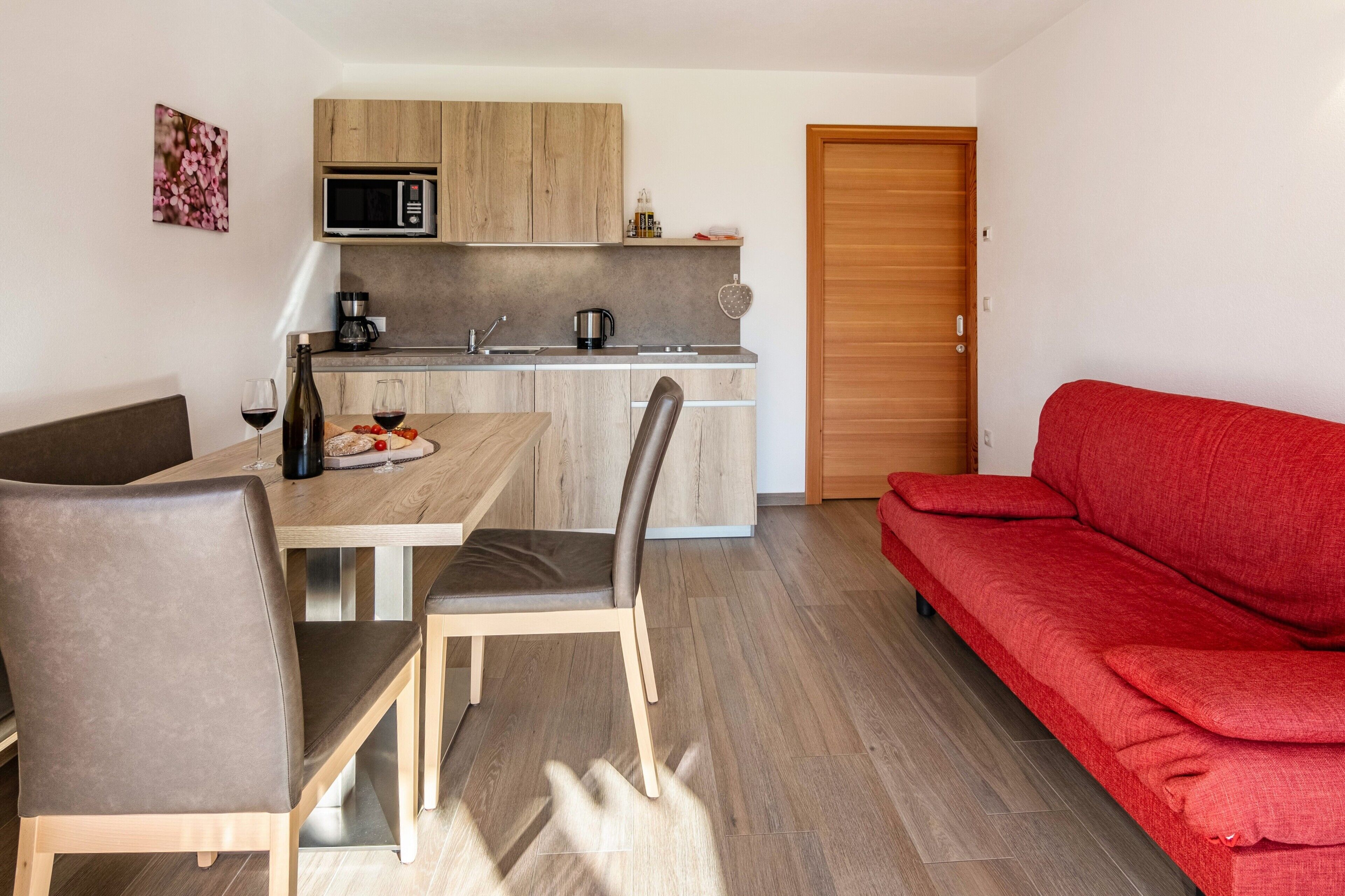 A compact living space with a dining area, kitchenette, and a red sofa.