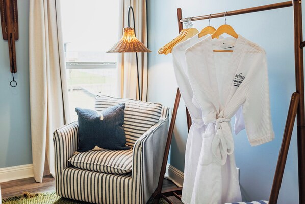 A striped armchair with a pillow, a white robe hanging on a wooden rack, and a pendant light.
