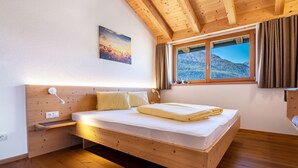 A wooden bed in a room with a window, a wall-mounted light, and a power outlet.
