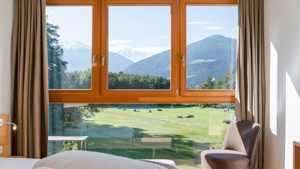 Ein Schlafzimmer mit großem Fenster, einem Bett, einem Stuhl und einem Tisch.