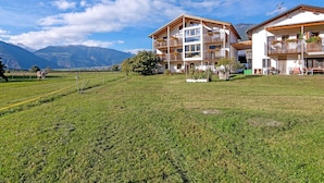 Ein Hotel mit mehreren Balkonen, einer Rasenfläche und einer Bergkulisse.