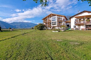 A hotel with multiple balconies, a grassy lawn, and a mountainous backdrop.
