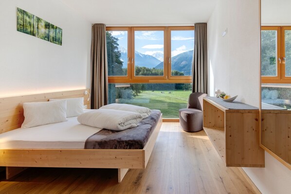 A bedroom with a wooden bed, a desk, and a view of mountains and a green field.