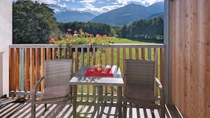Ein Balkon mit Korbstühlen, einem Tisch mit roter Unterlage und einer Flasche.