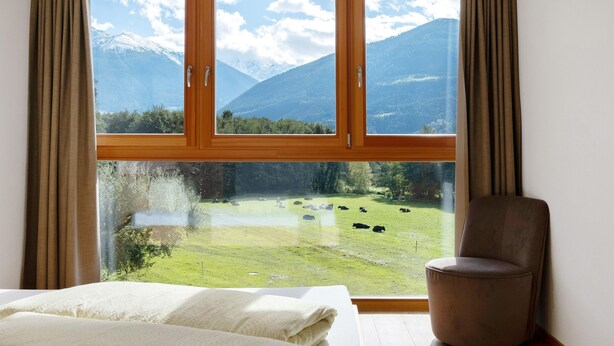 Ein Zimmer mit großem Fenster, einem Bett und einem Sessel.