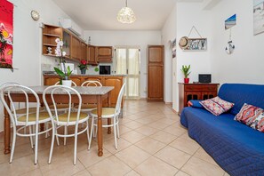 Una cocina con armarios de madera, una mesa de comedor con sillas, un sofá azul con cojines estampados y una lámpara colgante.