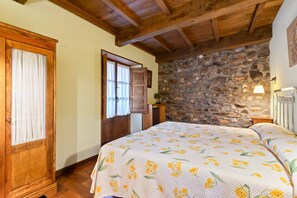 A bedroom with a bed, wooden door, stone wall, and a lamp.