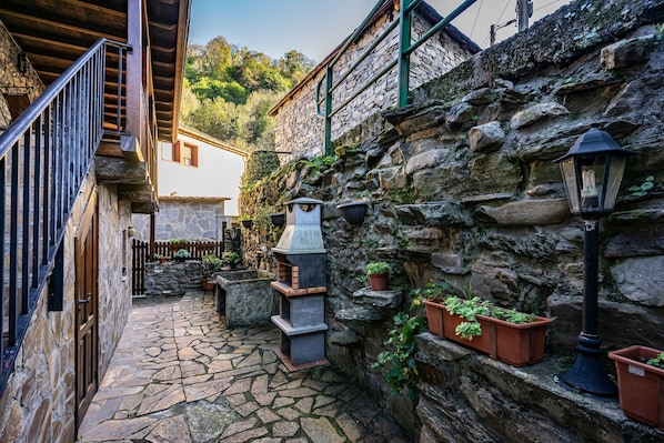 A stone-walled courtyard with a wooden staircase, a brick oven, and potted plants.
