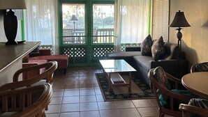 A spacious living room with a high ceiling fan, green-framed windows, a sofa set, a dining table, and a coffee table. - Ocean, freshness, vibe; 1 bedroom + loft + sofas. (Maunaloa)