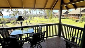 A covered outdoor seating area with a table and chairs, overlooking a grassy landscape with palm trees and houses. - Ocean, freshness, vibe; 1 bedroom + loft + sofas. (Maunaloa)