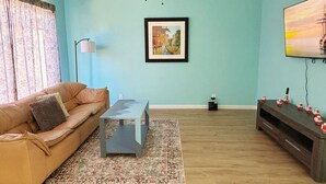 A living room with a brown sofa, a coffee table, a framed painting, a ceiling fan, and a TV on the wall. - Cozy 3BR Home Near SF & Napa Valley (Vallejo)