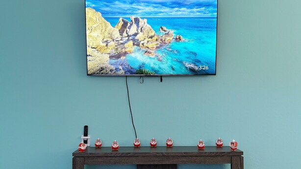 A television mounted on a teal wall displaying a coastal landscape. Below the TV, a wooden entertainment unit holds several figurines. - Cozy 3BR Home Near SF & Napa Valley (Vallejo)