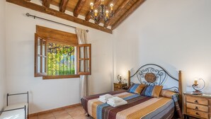 Een slaapkamer met een bed, een raam met gordijnen, een kroonluchter en een nachtkastje.