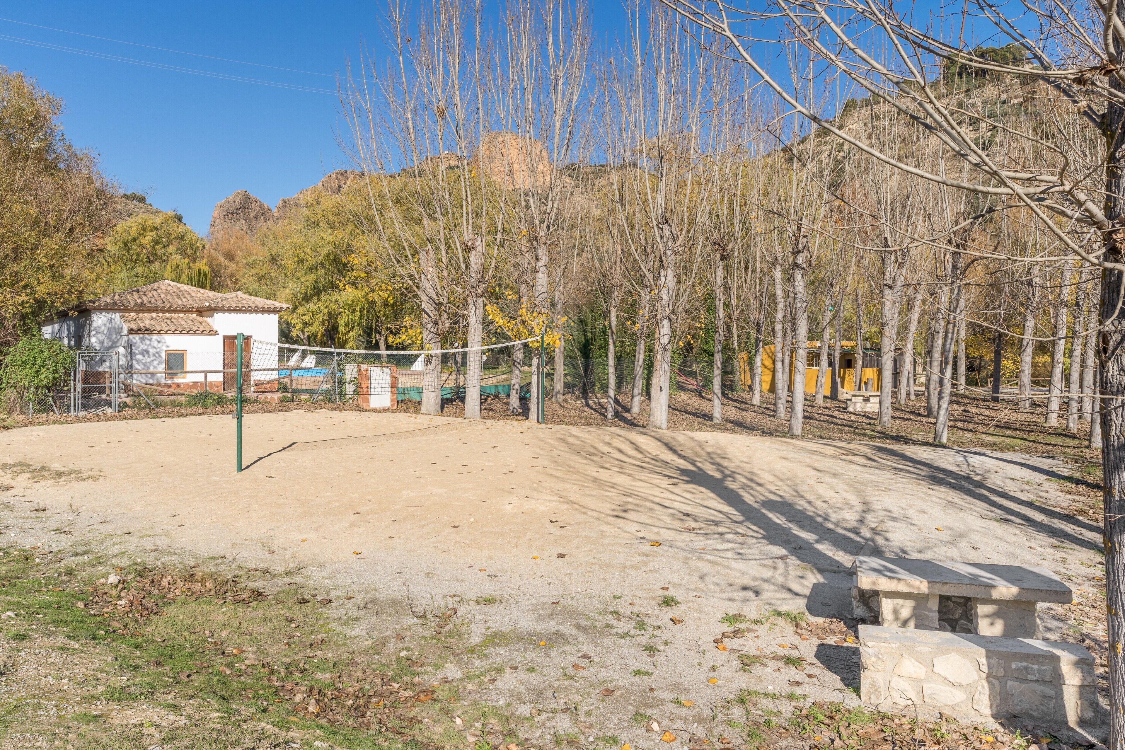 Una cancha de voleibol con una red, un banco de piedra y un edificio al fondo.