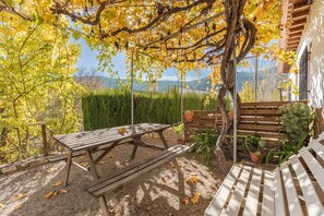 A wooden picnic table and bench in a garden with yellow foliage and a view of hills.