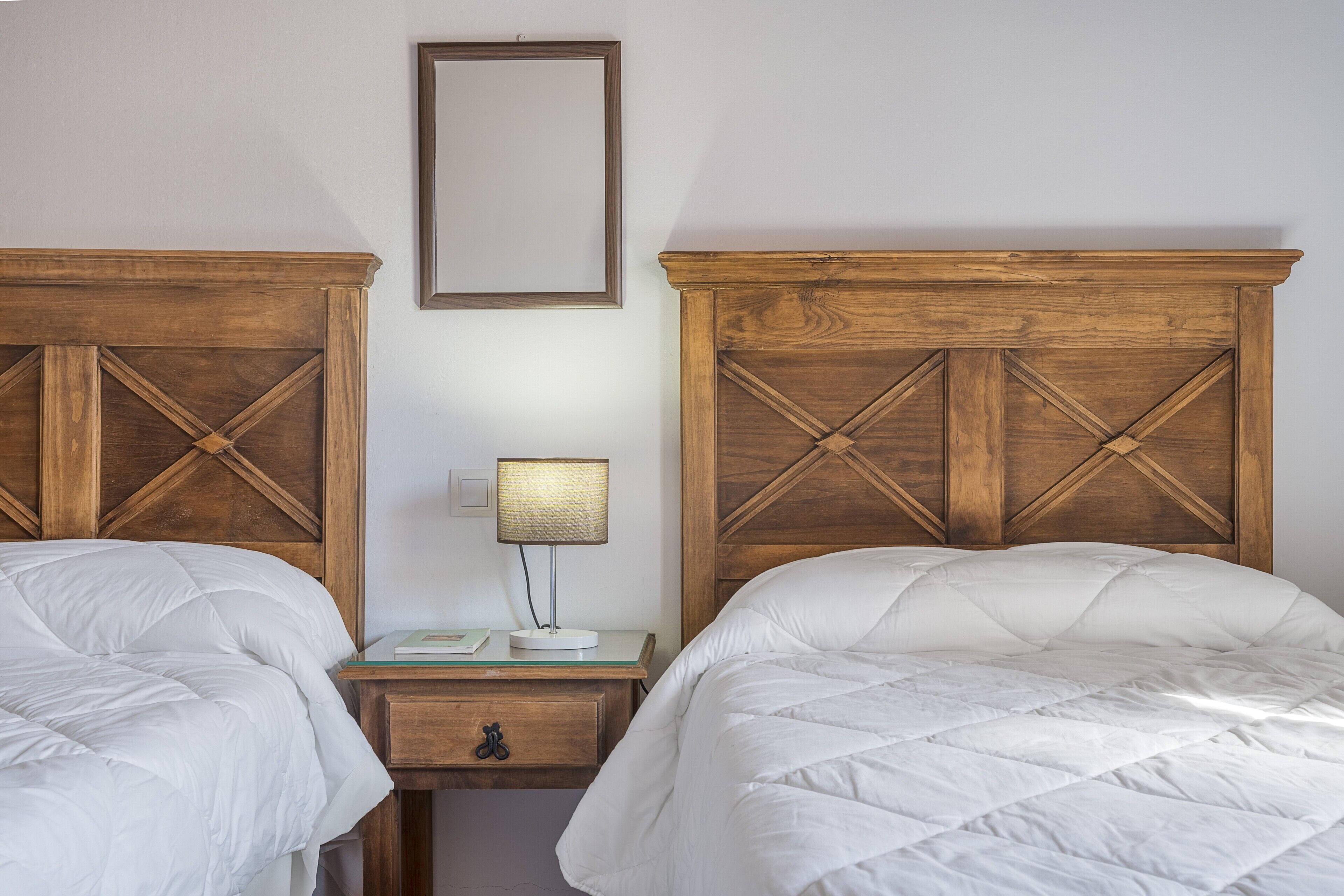 Un dormitorio con dos camas, una mesita de noche con lámpara y un espejo en la pared.