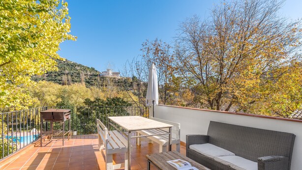 A terrace with a table, bench, and wicker sofa, overlooking a pool and trees. - Apartment 'Casa Rural Cortijo El Plantio' with Mountain View, Wi-Fi and Air Conditioning (Granada)