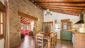 A stone-walled kitchen with a dining area, wooden chairs, a table, and a hanging light fixture. - Apartment 'Casa Rural Cortijo El Plantio' with Mountain View, Wi-Fi and Air Conditioning (Granada)