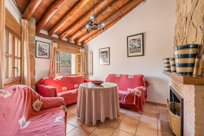 A cozy room with a fireplace, two red sofas, a round table, and wooden beams on the ceiling. - Apartment 'Casa Rural Cortijo El Plantio' with Mountain View, Wi-Fi and Air Conditioning (Granada)