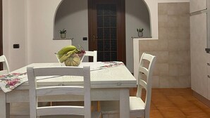 Een eetruimte met een witte tafel en stoelen, een betegelde vloer en een deur met raam.