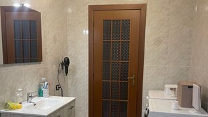 Een badkamer met een houten deur, een wastafel met spiegel, een wasmachine en een wasmand.