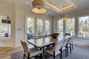 Une salle à manger avec une grande table en bois, six chaises rembourrées et deux lampes suspendues.
